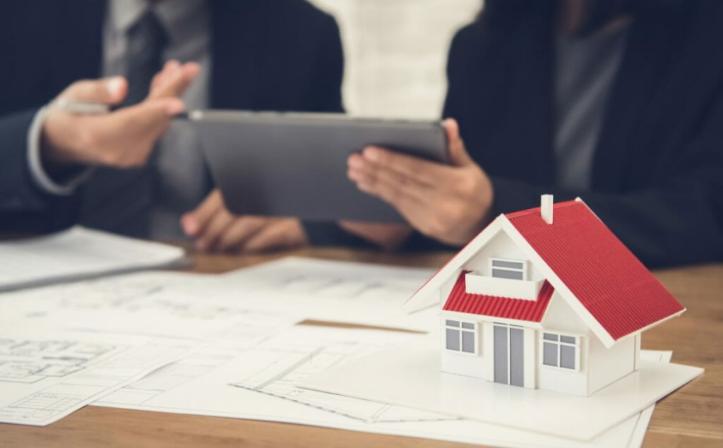Two men in suits discussing property plans at a desc with a model house