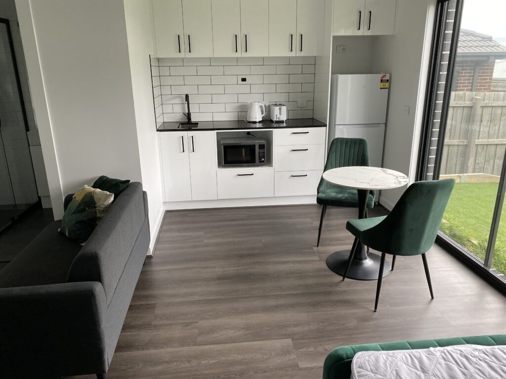 Co-Living studio with kitchenette, dining area, private yard, and partial view of bed and ensuite