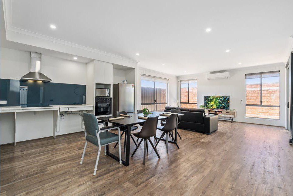 Open-plan living area in an NDIS property with a modern kitchen, dining table, and cozy sofa, designed for participant comfort